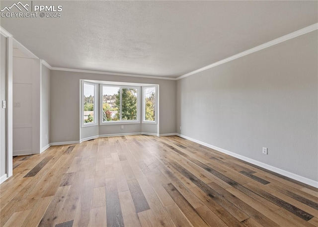 spare room featuring light hardwood / wood-style floors, crown molding, and a textured ceiling