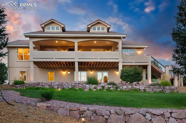 back house at dusk featuring a balcony and a yard