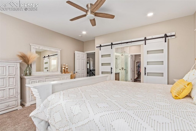 carpeted bedroom with a barn door, a walk in closet, and ceiling fan