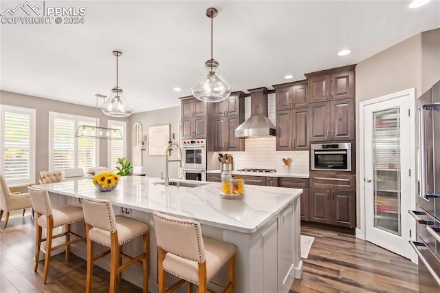 kitchen featuring a large island with sink, wall chimney range hood, dark hardwood / wood-style flooring, and hanging light fixtures