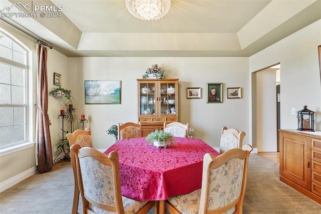 dining area featuring a tray ceiling, light carpet, and a notable chandelier