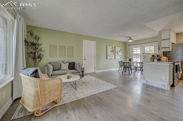 living room featuring light wood-type flooring, ceiling fan, and a textured ceiling