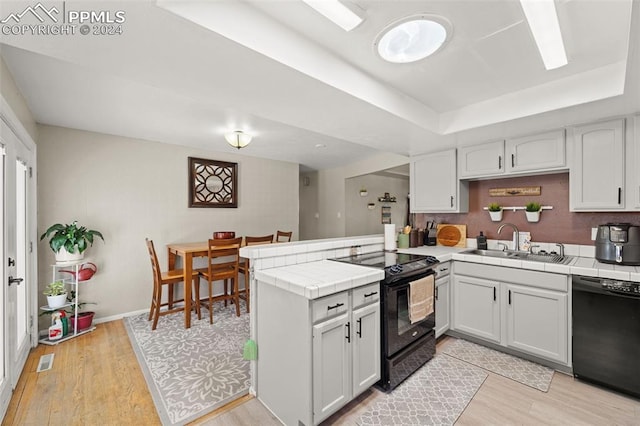 kitchen with black appliances, white cabinets, kitchen peninsula, and tile countertops