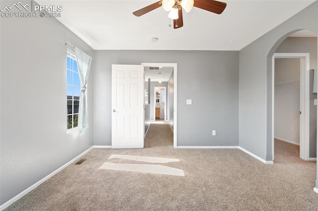 unfurnished bedroom featuring a spacious closet, a closet, light colored carpet, and ceiling fan