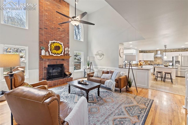 living room with a fireplace, a high ceiling, ceiling fan, and light hardwood / wood-style floors