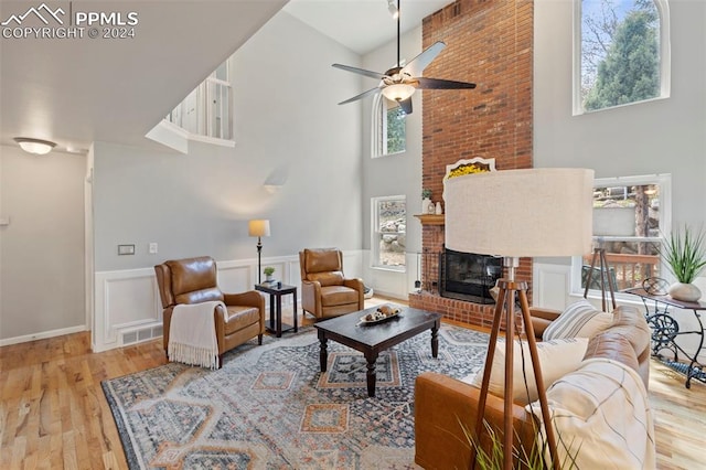 living room with a brick fireplace, light hardwood / wood-style flooring, ceiling fan, and a high ceiling