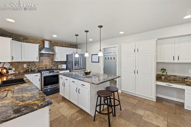 kitchen with a kitchen island, wall chimney exhaust hood, appliances with stainless steel finishes, sink, and white cabinetry