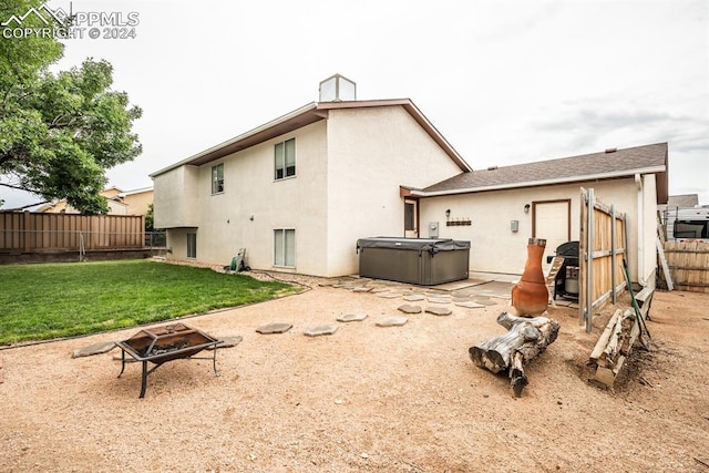 rear view of property with an outdoor fire pit, a patio area, a yard, and a hot tub