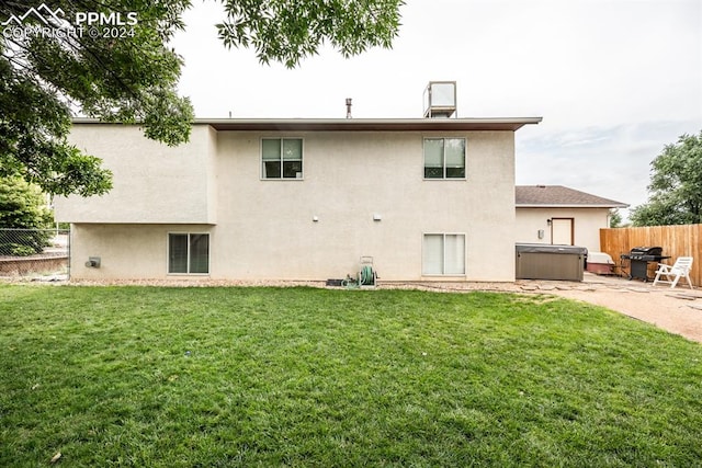 back of property featuring a hot tub, a lawn, and a patio area