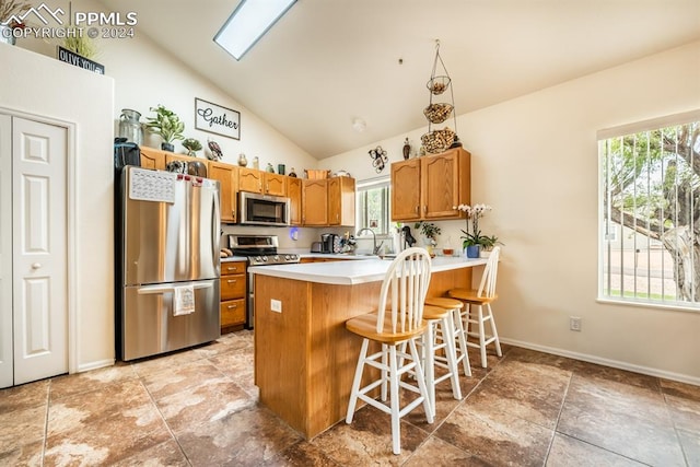 kitchen with vaulted ceiling with skylight, a kitchen bar, stainless steel appliances, kitchen peninsula, and sink