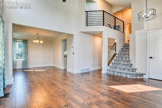 unfurnished living room featuring crown molding, a towering ceiling, dark wood-type flooring, and a notable chandelier