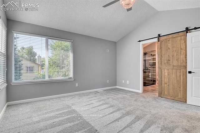 unfurnished bedroom featuring lofted ceiling, a barn door, ceiling fan, and multiple windows