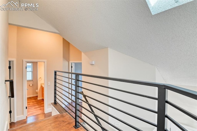 hallway featuring a textured ceiling, light hardwood / wood-style floors, and lofted ceiling with skylight