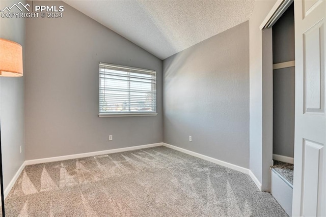 unfurnished bedroom with a textured ceiling, carpet flooring, and lofted ceiling