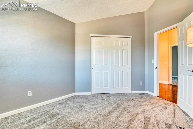 unfurnished bedroom featuring a textured ceiling, a closet, carpet floors, and lofted ceiling