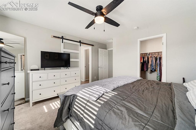 carpeted bedroom featuring a barn door, ceiling fan, a closet, and a spacious closet