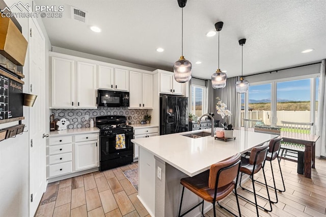 kitchen with black appliances, pendant lighting, a center island with sink, and white cabinetry