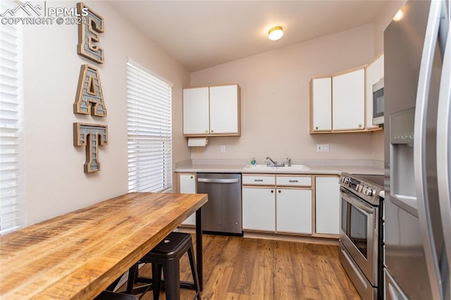 kitchen featuring light wood-type flooring, sink, white cabinets, lofted ceiling, and stainless steel appliances