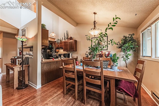 dining area featuring lofted ceiling, hardwood / wood-style floors, a baseboard heating unit, and a textured ceiling