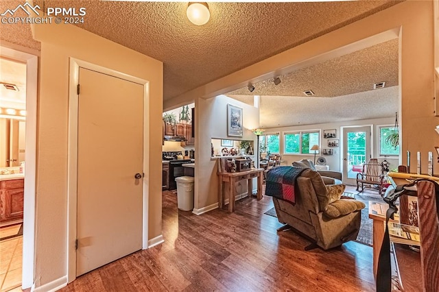 living room with a textured ceiling, vaulted ceiling, and wood-type flooring