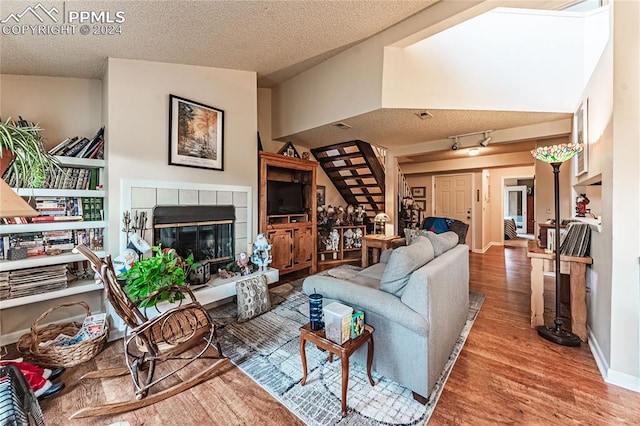 living room featuring a textured ceiling, vaulted ceiling, a tiled fireplace, and hardwood / wood-style floors