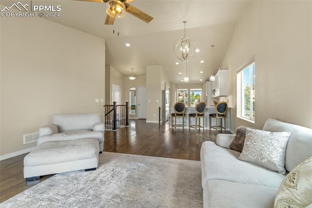 living room with dark hardwood / wood-style flooring, ceiling fan with notable chandelier, and high vaulted ceiling