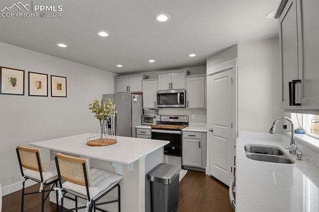 kitchen with sink, gray cabinets, stainless steel appliances, a kitchen bar, and dark hardwood / wood-style flooring