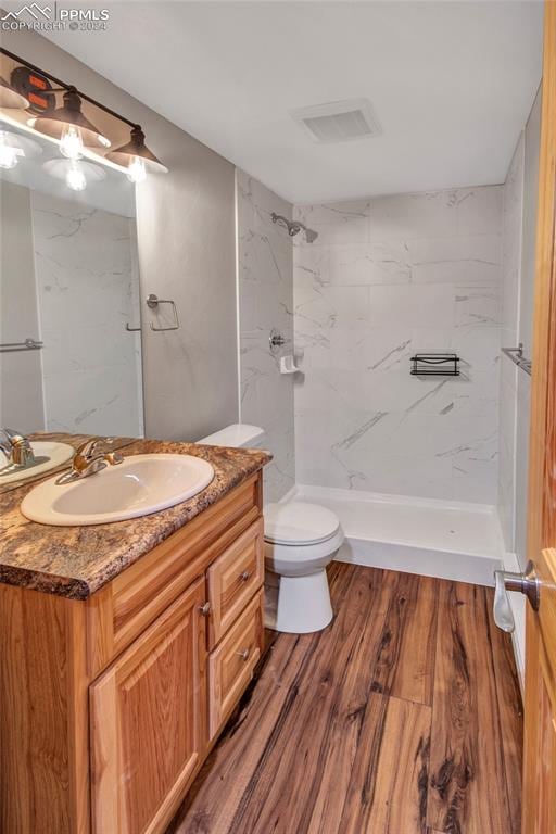 bathroom with tiled shower, wood-type flooring, toilet, and vanity