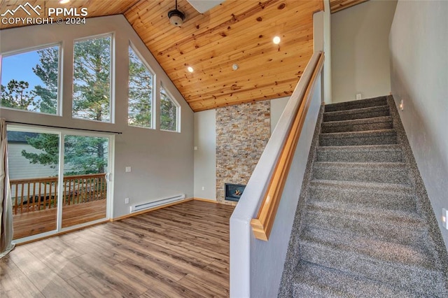 stairway with hardwood / wood-style floors, wood ceiling, baseboard heating, a stone fireplace, and high vaulted ceiling