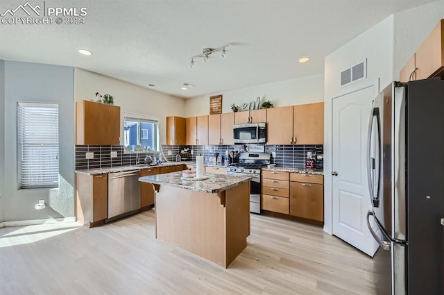 kitchen with tasteful backsplash, light stone counters, a kitchen island, stainless steel appliances, and light hardwood / wood-style floors