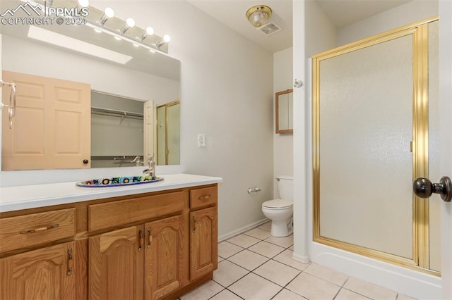 bathroom featuring toilet, tile patterned flooring, a shower with door, vanity, and a skylight