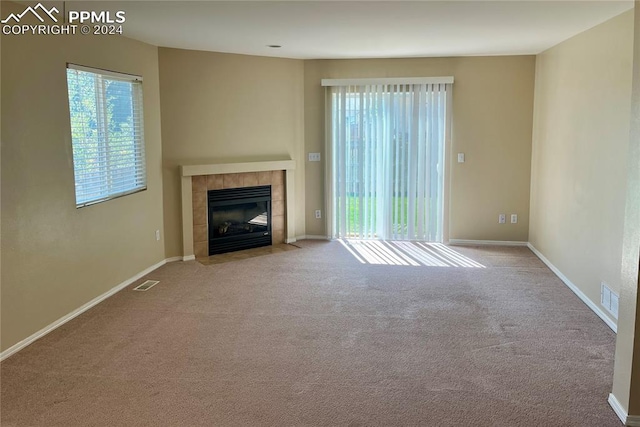 unfurnished living room featuring light colored carpet and a tiled fireplace