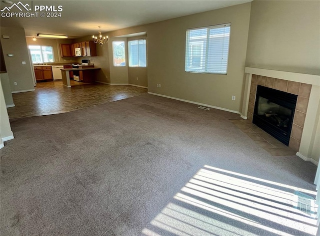 unfurnished living room featuring a tiled fireplace, plenty of natural light, an inviting chandelier, and carpet