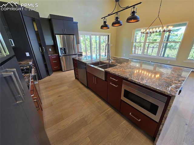 kitchen featuring light hardwood / wood-style flooring, decorative light fixtures, appliances with stainless steel finishes, sink, and an island with sink