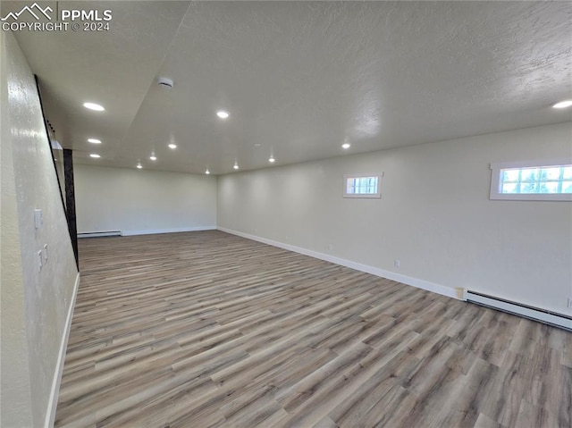 basement with a textured ceiling, a baseboard radiator, and light hardwood / wood-style floors