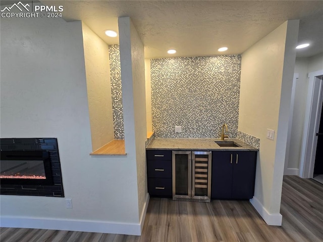 bar featuring a textured ceiling, dark hardwood / wood-style flooring, beverage cooler, tasteful backsplash, and sink