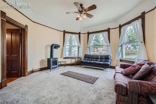 carpeted living room with a wood stove, ceiling fan, and a textured ceiling