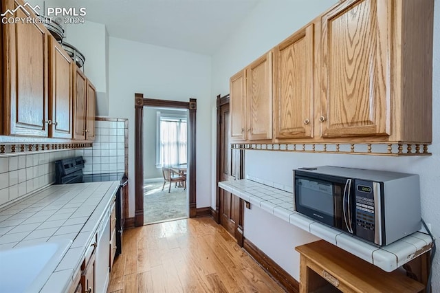 kitchen featuring tile countertops, decorative backsplash, range with electric stovetop, and light hardwood / wood-style flooring