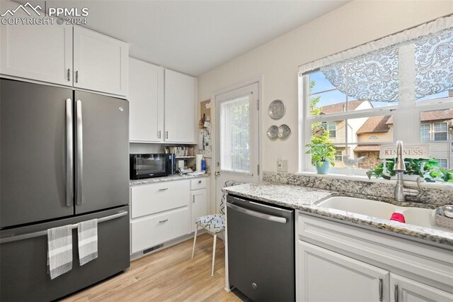 kitchen with white cabinets, light wood-type flooring, appliances with stainless steel finishes, light stone counters, and sink