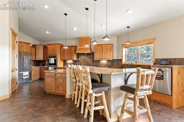 kitchen featuring backsplash, stainless steel appliances, light stone counters, hanging light fixtures, and a center island with sink