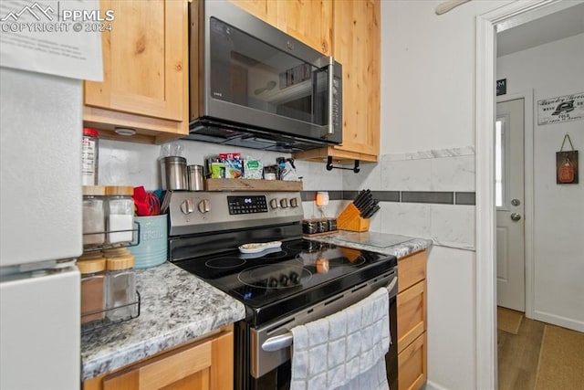 kitchen with light brown cabinetry, hardwood / wood-style flooring, light stone countertops, stainless steel appliances, and tasteful backsplash