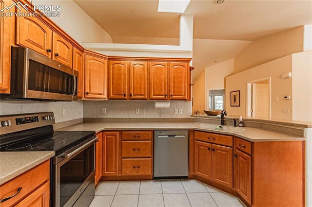 kitchen featuring light tile patterned floors, light stone countertops, vaulted ceiling, sink, and stainless steel appliances