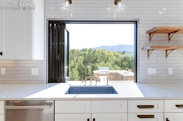 kitchen with white cabinets, light stone countertops, stainless steel dishwasher, a mountain view, and sink