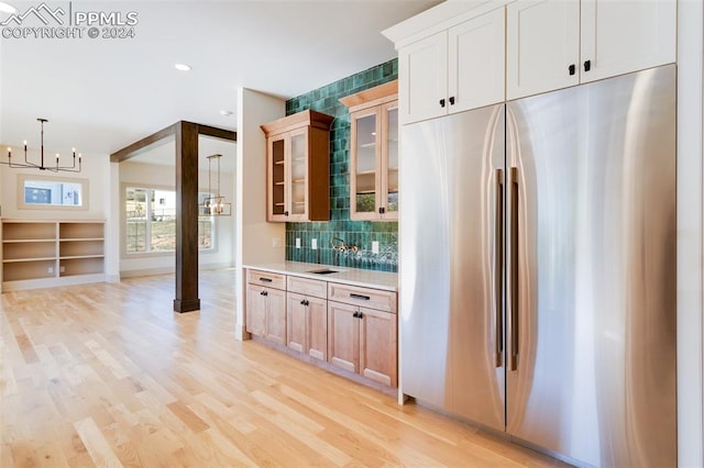 kitchen with stainless steel built in fridge, decorative light fixtures, a chandelier, light hardwood / wood-style floors, and tasteful backsplash