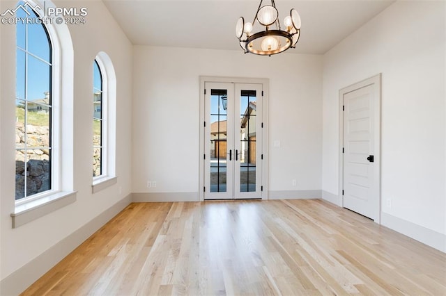 spare room with french doors, light hardwood / wood-style floors, and an inviting chandelier