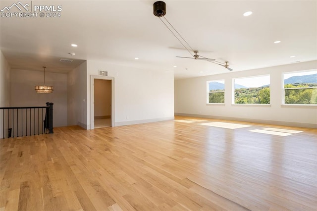 empty room featuring light wood-type flooring and ceiling fan with notable chandelier