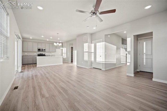 unfurnished living room with ceiling fan with notable chandelier, sink, and light hardwood / wood-style floors