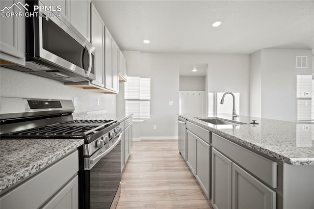 kitchen featuring light hardwood / wood-style flooring, appliances with stainless steel finishes, light stone countertops, sink, and a kitchen island with sink