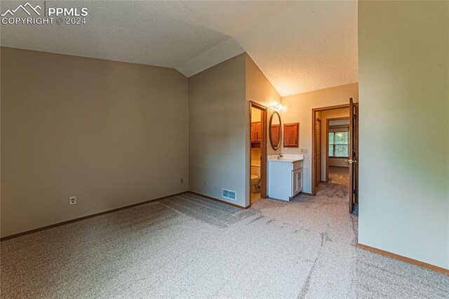 unfurnished bedroom with a textured ceiling, vaulted ceiling, connected bathroom, sink, and light colored carpet