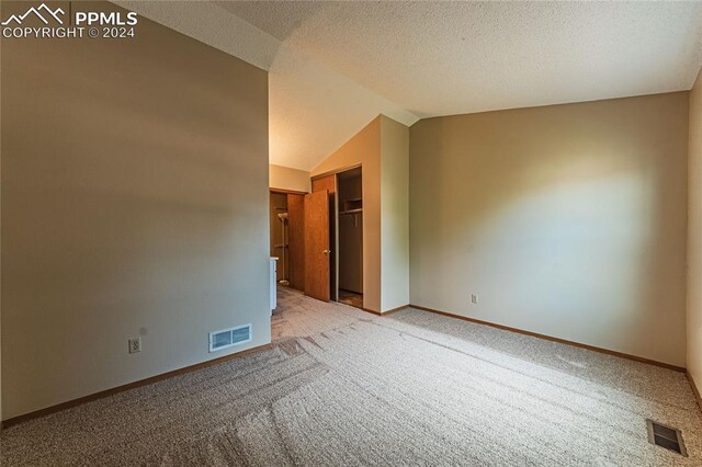 carpeted spare room featuring a textured ceiling and vaulted ceiling